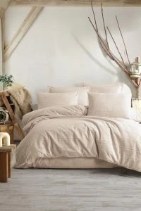 Mekani i udobni jorgan i jastuci u bež boji, idealni za boho stil spavaće sobe, izrađeni od 100% pamuka, sa teksturom za dodatnu eleganciju i udobnost.