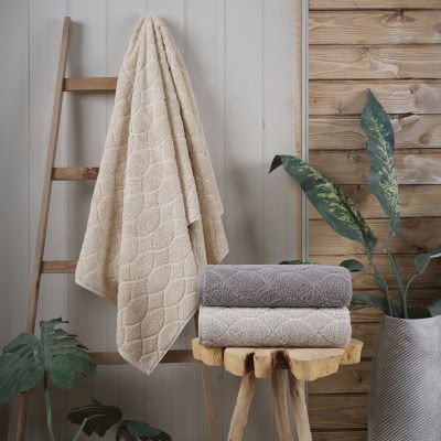 Nadmorski peškir za ruke i tijelo, 50x90cm, u bež boji, prikazan na drvenoj stalki s drugim ručnicima, idealan za kupaonicu ili spa prostor, visok kvalitet i mekanost.
