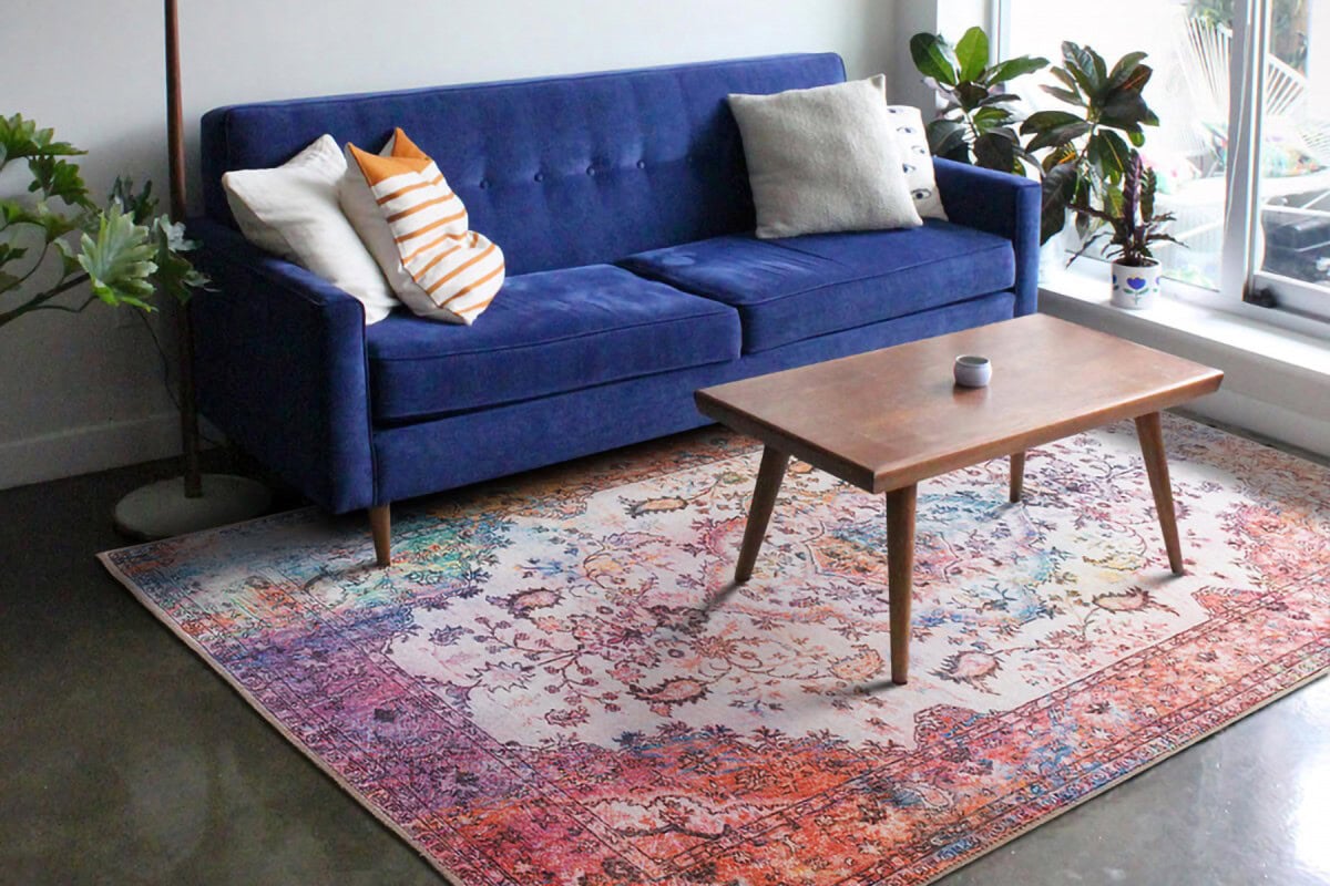 Niska, moderna plava sofa s ukrasnim jastucima u dnevnom boravku s tepihom i biljkama, idealno za udobno i stilizirano sjedenje.