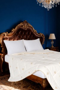 Vuna jorgan na krevetu sa elegantnim drvenim uzglavljem i plavom zidnom pozadinom, idealan za udoban san i dekorativni izgled spavaće sobe.